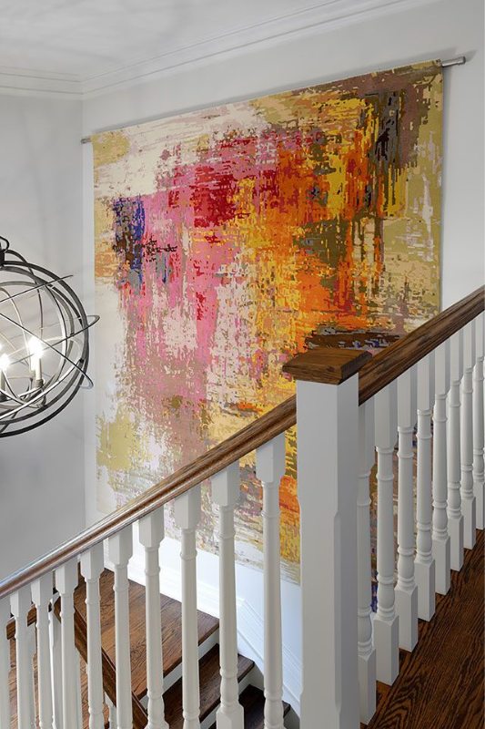 Large colorful abstract artwork displayed on a tall staircase wall with white railings
