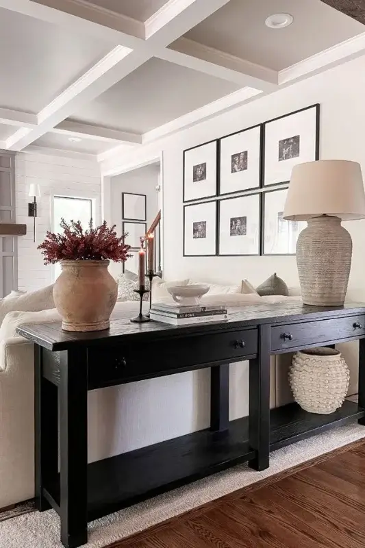 Black console table behind a cream sofa styled with ceramic vases, framed black and white art, table lamps, and woven baskets for elegant sofa table decor ideas