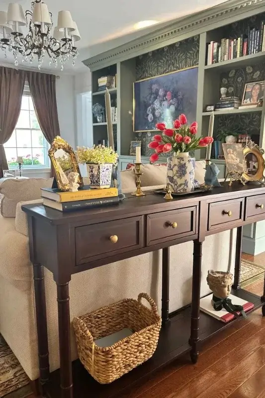 Dark wood console table behind sofa decorated with tulips, vintage frames, books, and woven baskets for traditional living room sofa table styling