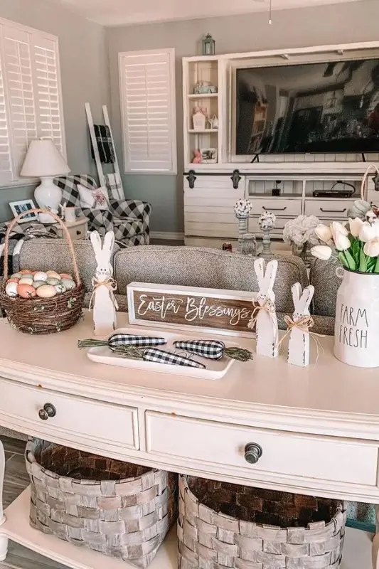 Farmhouse sofa table behind couch decorated for Easter with wooden bunny figurines, eggs, gingham accents, tulips, and woven baskets for seasonal console table styling