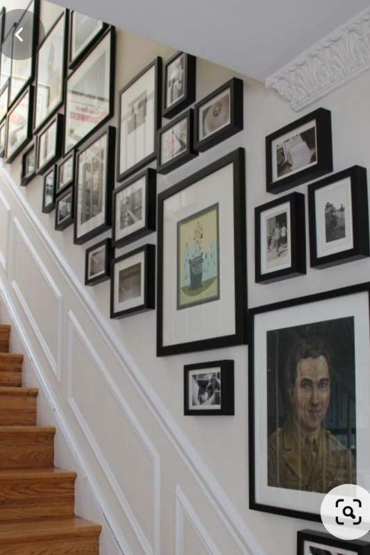 Eclectic staircase gallery wall with mixed black frames arranged above decorative white wall molding
