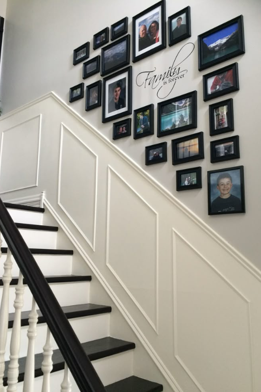 Family photo gallery wall with black frames arranged along a staircase with white picture frame molding