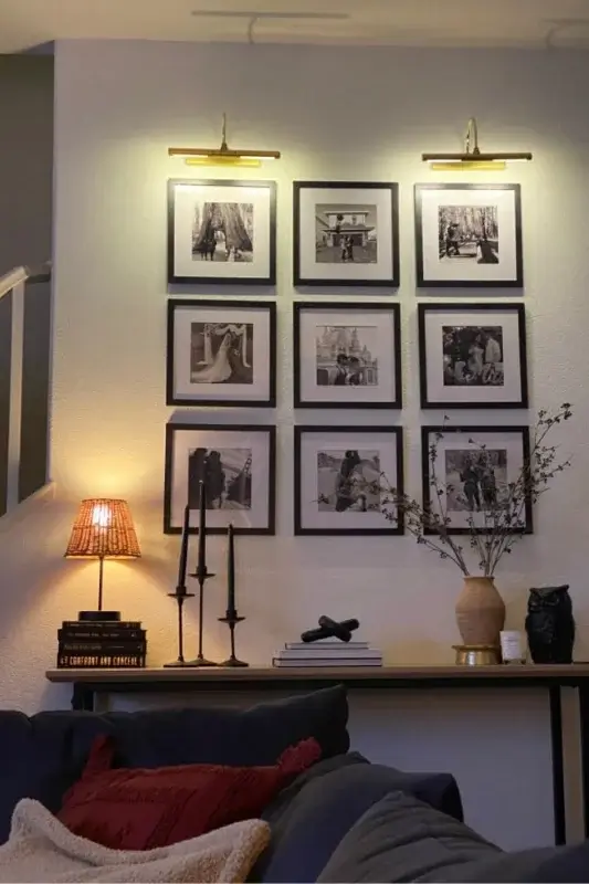 Console table behind sofa styled with black candlesticks, table lamp, books, and a black and white gallery wall for classic behind the couch decor ideas