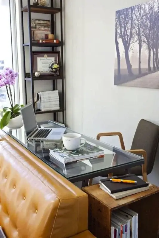 Glass desk behind sofa used as a small home office setup with laptop, books, chair, and shelving for functional behind the couch workspace ideas