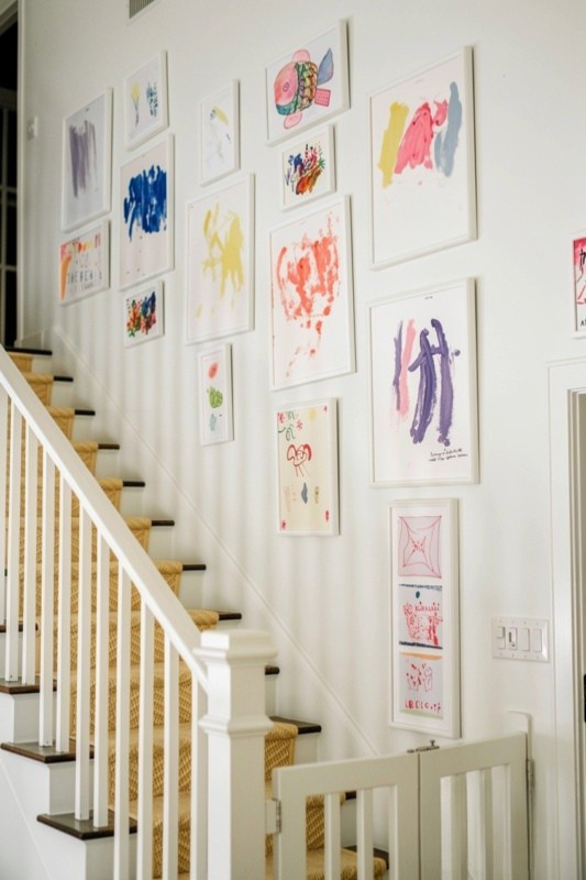 Children's colorful artwork displayed in white frames along a bright staircase wall