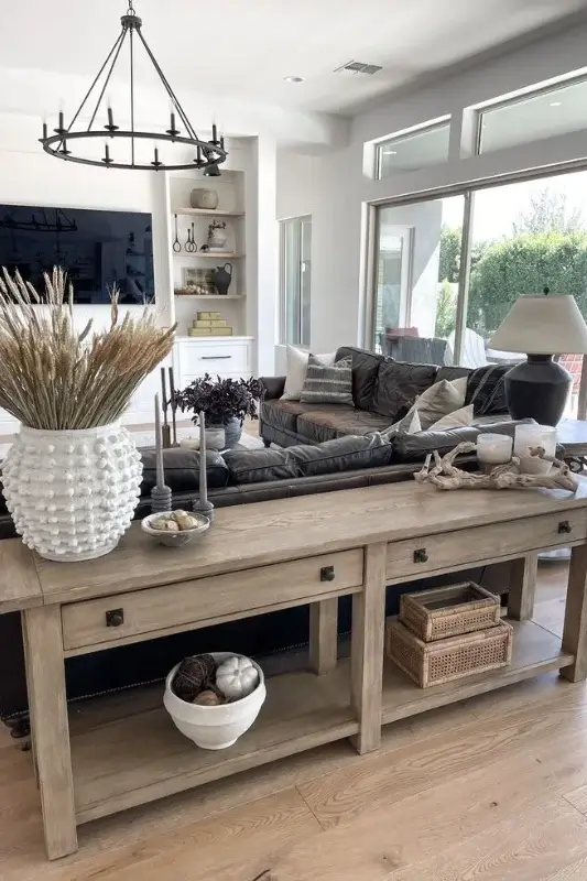 Large wood console table behind a dark leather sofa styled with neutral vases, candles, baskets, and layered decor in an open concept living room