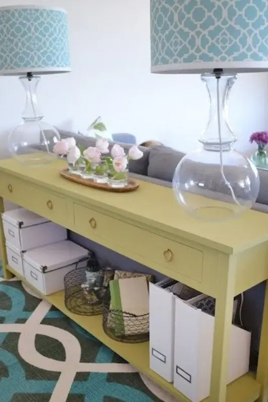 Lime green console table behind sofa styled with matching glass lamps, decorative boxes, baskets, and floral accents for colorful sofa table decor ideas