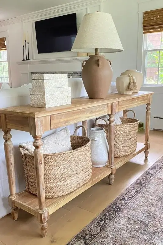 Natural wood console table behind sofa styled with woven baskets, pillows, ceramic vases, and neutral accents for cozy sofa table decor