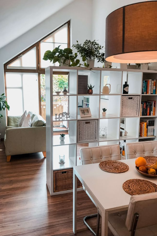 Minimalist studio apartment with a black-framed glass partition separating the bed from the living area, maximizing light and privacy in a small space.