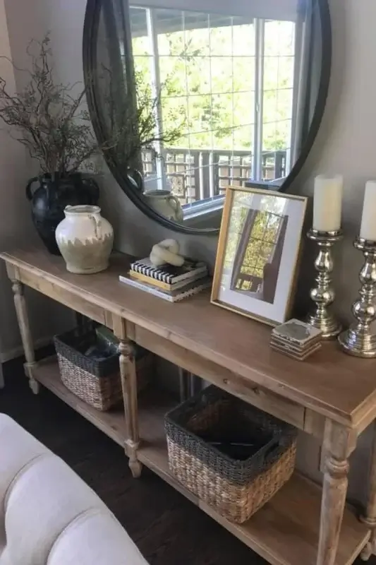 Console table behind sofa styled with a round mirror, framed art, candlesticks, books, and woven baskets for classic living room decor ideas