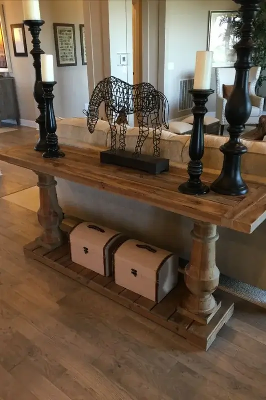 Rustic wood console table behind sofa styled with black candlesticks, metal horse sculpture, and storage trunks for bold sofa table styling