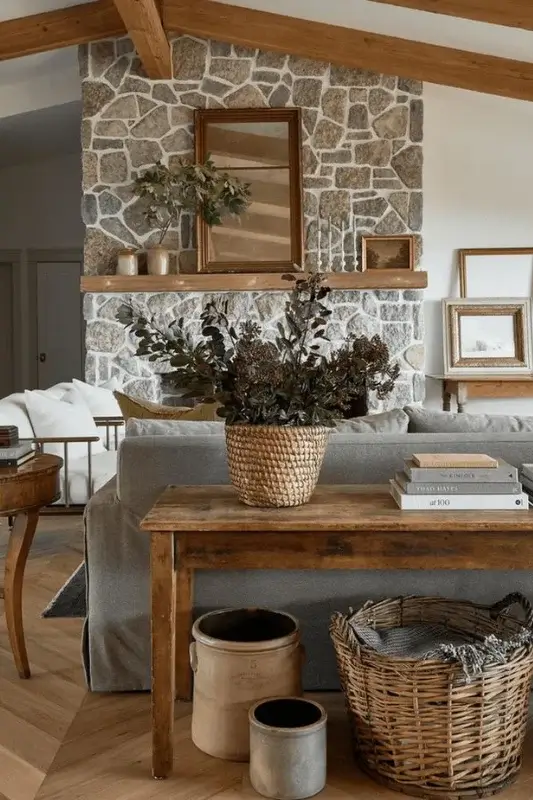 Rustic wood console table behind sofa styled with a woven basket, pottery, stacked books, and greenery for warm farmhouse living room decor