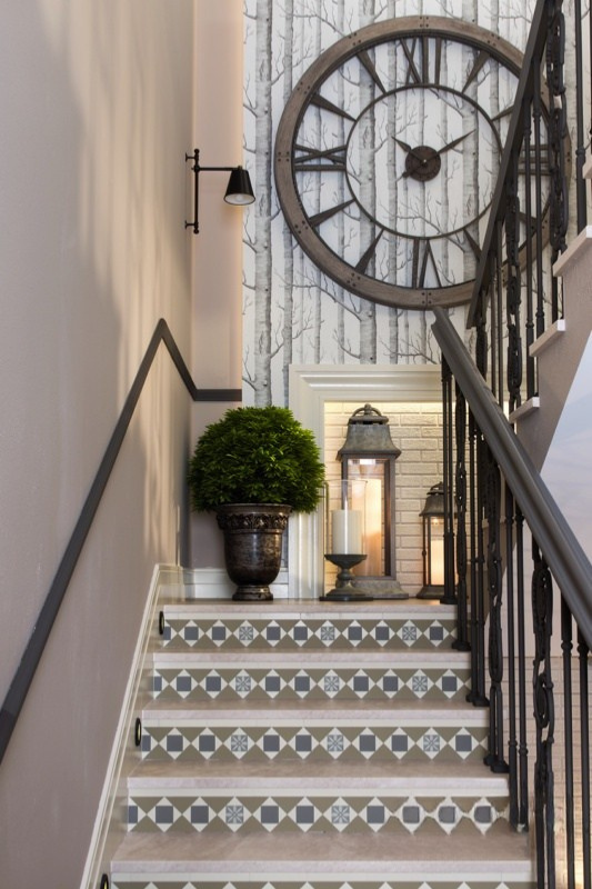 Staircase wall decorated with an oversized vintage clock, botanical wallpaper, lanterns, and greenery