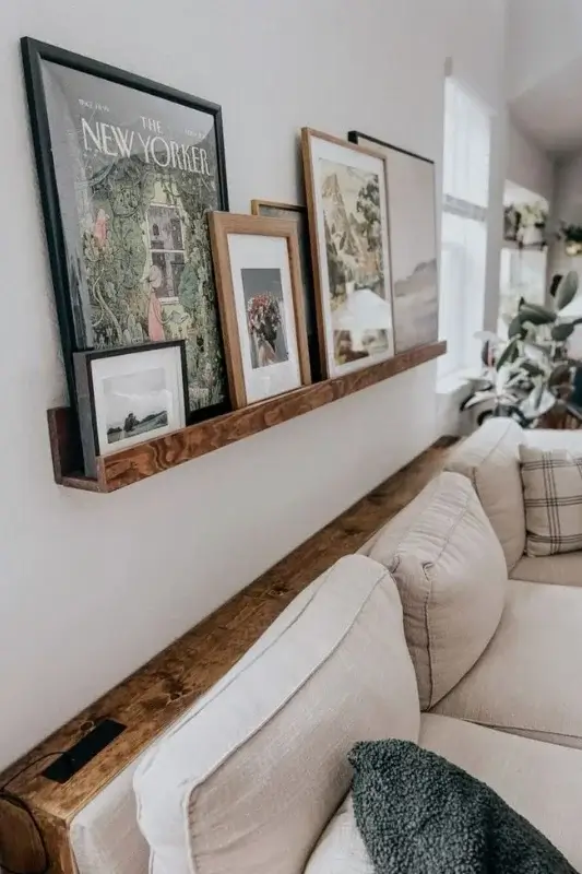 Wood picture ledge shelf behind sofa styled with framed artwork and prints for simple and space saving behind the couch wall decor
