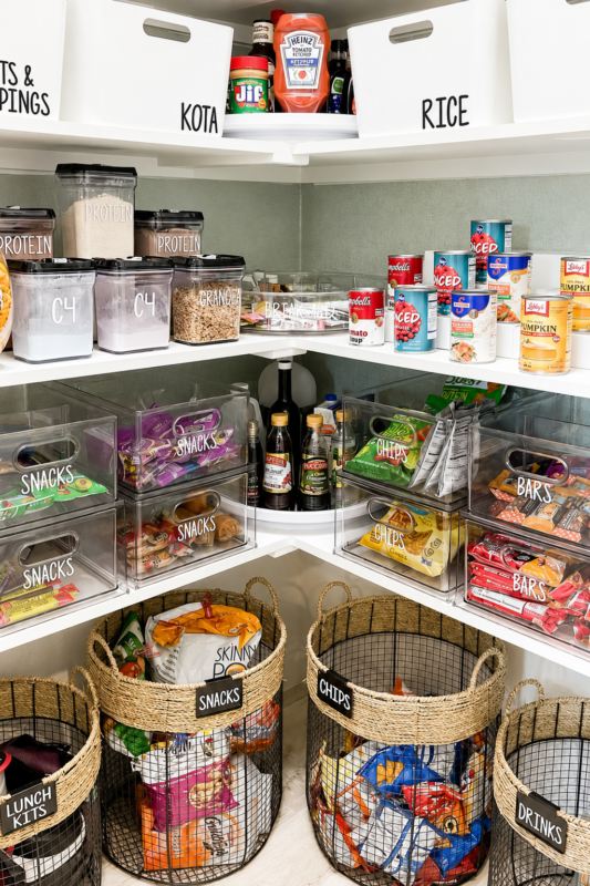White pantry shelves organized with wire baskets, glass jars, cereal containers and kitchen storage risers.
