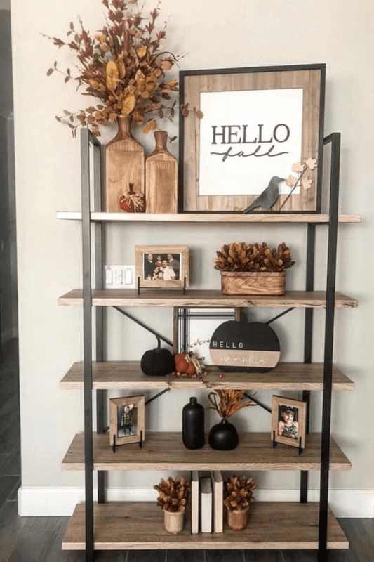 Open shelves styled with a Hello Fall sign, autumn foliage, pumpkins, wood accents, and framed photos