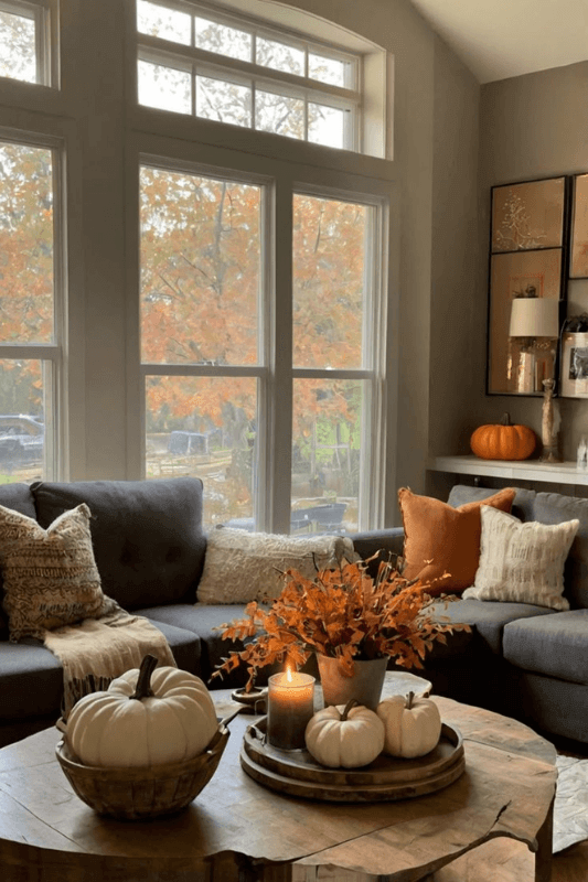 Neutral fall living room decor with white pumpkins, orange branches, cozy pillows, and a rustic wood coffee table