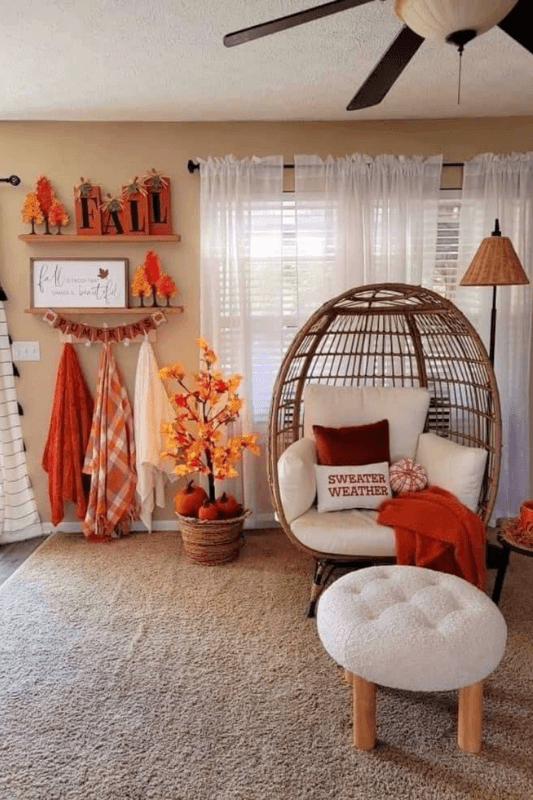 Cozy fall reading nook with a rattan chair, orange throw, fall pillows, pumpkins, and autumn foliage