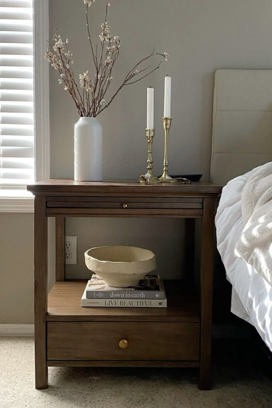 Wooden bedside table with brass candlesticks, ceramic vase, and books styled in a warm and earthy modern bedroom.