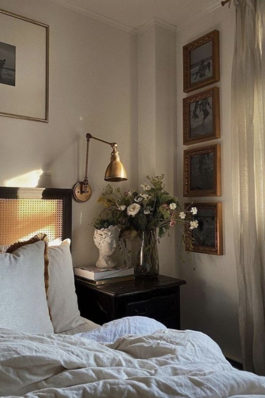 Vintage dark nightstand with wall-mounted lamp, classical bust, and floral arrangement in a moody romantic bedroom.