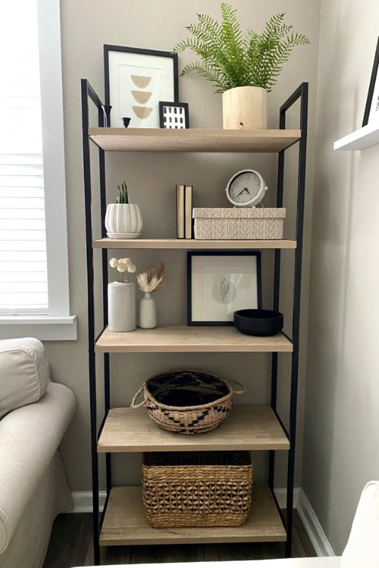 Minimalist black metal shelf featuring woven baskets, framed prints, small plants, and ceramic decor for a compact living space.