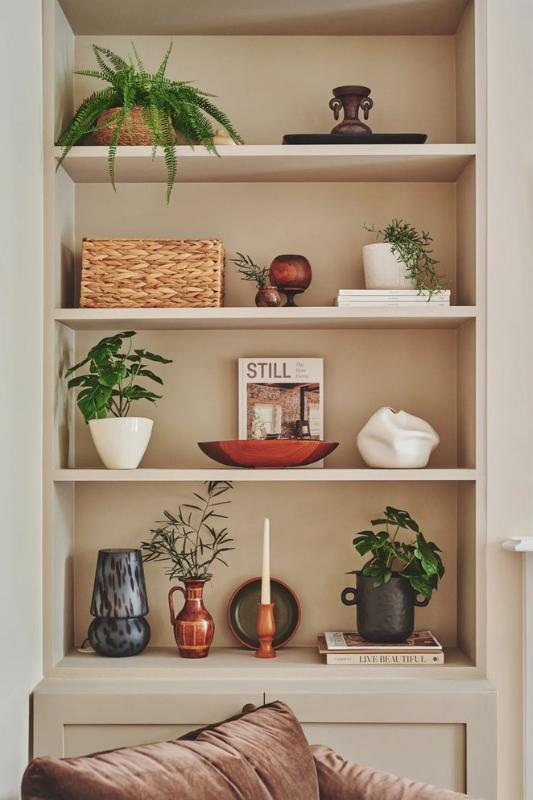 Built-in wooden shelves filled with textured ceramics, greenery, books, and woven baskets styled in a layered farmhouse aesthetic.