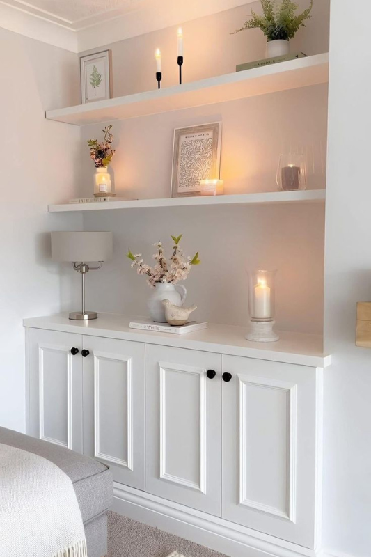 White custom built-in shelves styled with framed art, LED candles, florals, and warm lighting for a cozy traditional living room.