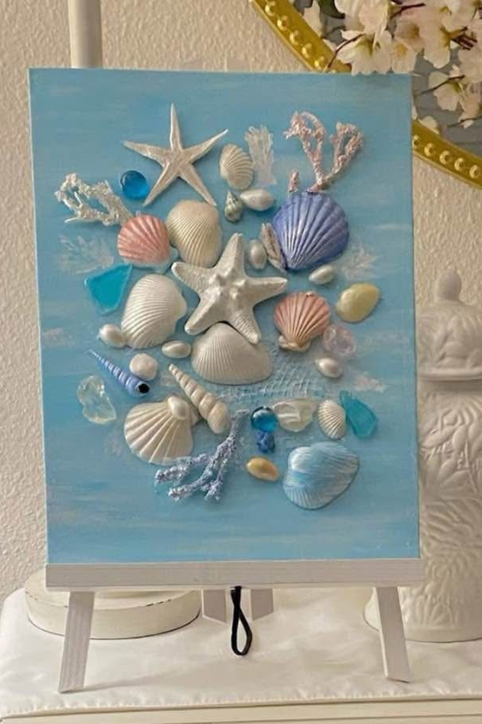 Seashell wall art arranged on a painted canvas for a beach themed summer DIY craft