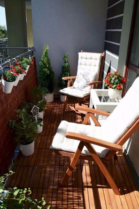 Small balcony with wooden deck tiles, white chairs, and potted plants styled like an outdoor lounge