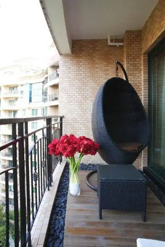 Balcony with hanging egg chair, statement flowers, and wood flooring for a luxury apartment vibe
