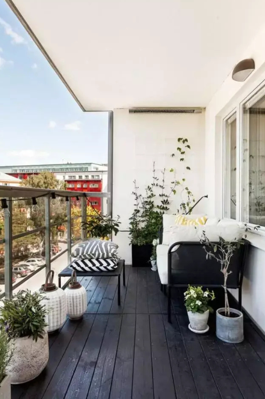 Modern small balcony with black flooring, minimal furniture, and greenery for a clean expensive aesthetic