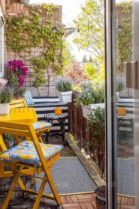 Small balcony seating area with bold accent chairs, outdoor rug, and potted plants for stylish apartment living