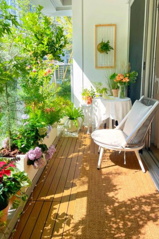 Small apartment balcony with lush greenery, wood flooring, and a cozy chair creating an expensive outdoor retreat