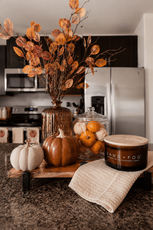 Amber vase with orange branches and mini pumpkins on a wooden kitchen island tray