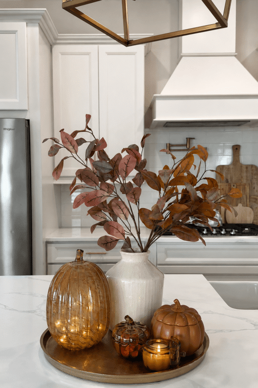 Fall kitchen island centerpiece with amber glass pumpkin, autumn branches, decorative pumpkins, and a glowing candle