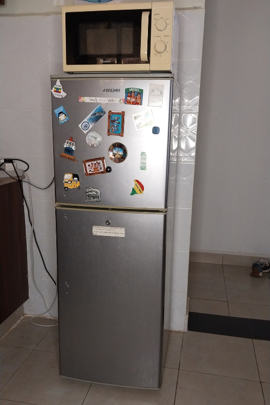 Cluttered fridge with travel magnets and microwave before fridge decor makeover