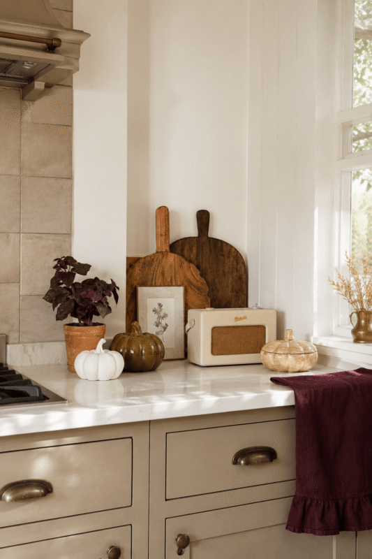 Simple fall kitchen counter with wooden cutting boards, decorative pumpkins, potted plant, and burgundy kitchen towel