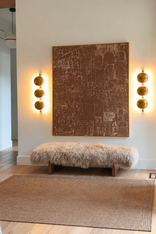 Pair of warm wall sconces highlighting large artwork above a textured bench
